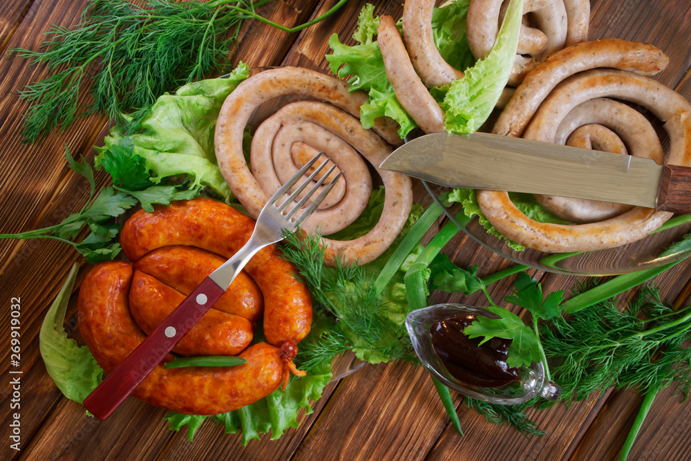 Grilled pork sausages, knife, fork, sauce in a sauce-pan and corn buns on a wooden surface of pine boards. Nearby are lettuce, dill and onion. Picnic - barbecue Grilled pork sausages, knife, fork, sauce in a sauce-pan and corn buns on a wooden surface of pine boards. Nearby are lettuce, dill and onion. Picnic - barbecue