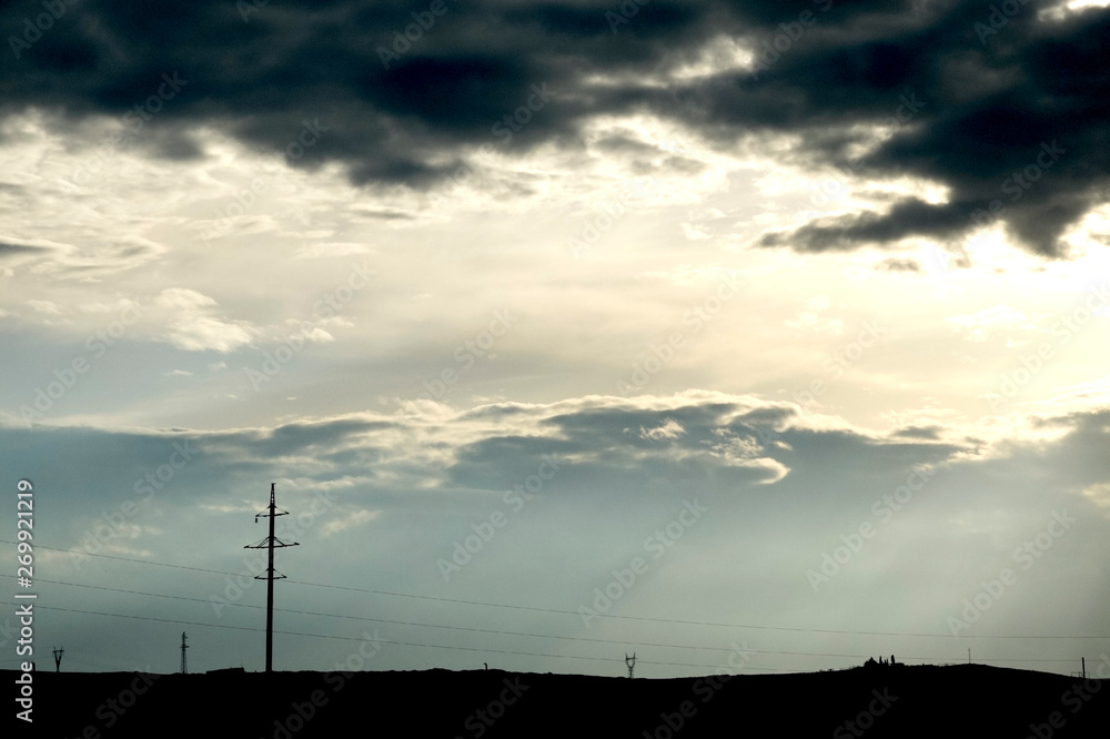 High voltage electricity poles. Pylons at dusk. Dramatic view of dark clouds at sunset.
