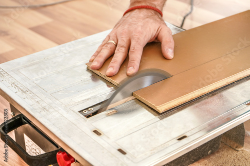 Man cutting laminate floor boards on circular saw, detail on hands holding wooden panel
