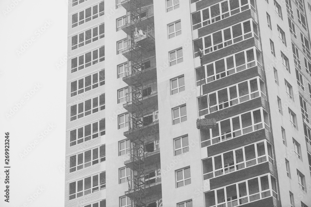 Monochrome concept of apartment building under construction close-up. Exterior of new multi-story residential building in grayscale. Background with walls, plastic windows and loggias. Copy space.