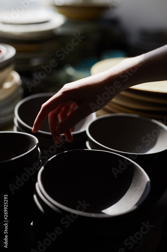Close-up of unrecognizable woman pointing at black ceramic bowl in crockery store, bowls stacking on shelf