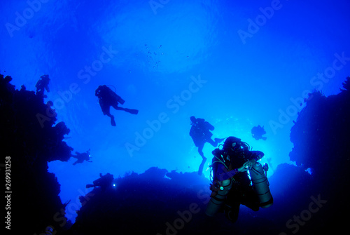 A silhouette shot of scuba divers using rebreather equipment are captured here just about to descend to depths of up to 300 feet. The shot was taken at the top of the wall in the Cayman Islands