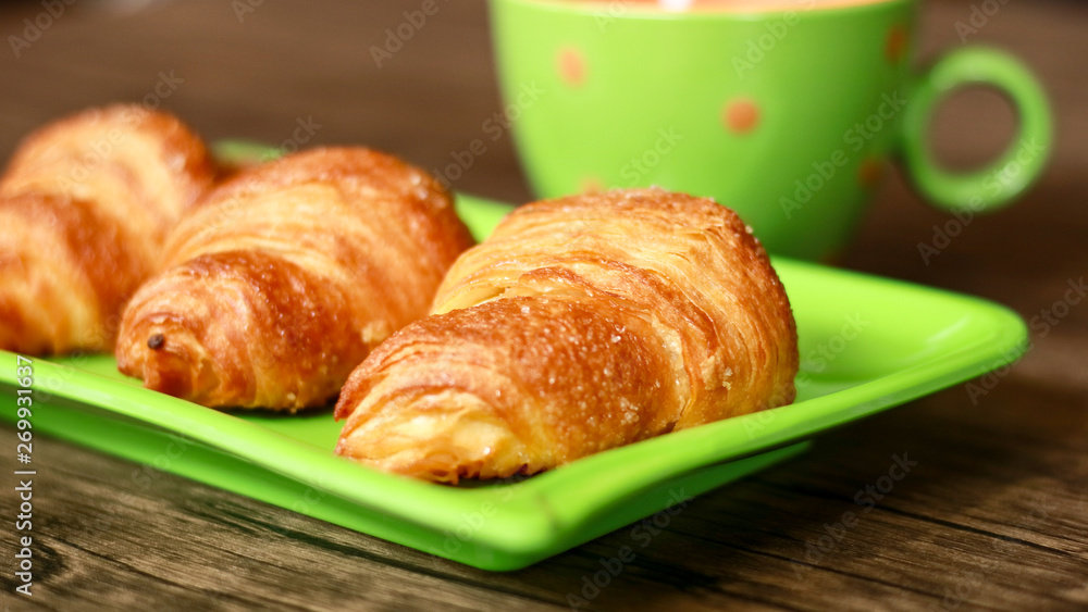 Croissants on green plate and a cup of drink. Wood background. 