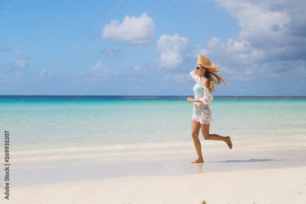 Sexy tanned girl in blue bikini and white tunica running on the seashore. Beautiful model sunbathes and rests on sea. Concept vacation, travel Sexy tanned girl in blue bikini and white tunica running on the seashore. Beautiful model sunbathes and rests on sea. Concept vacation, travel