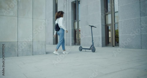 Wallpaper Mural Attractive African American black female uses her phone to unlock and rent an electric city shared scooter. 4K UHD 60 FPS SLOW MOTION Torontodigital.ca