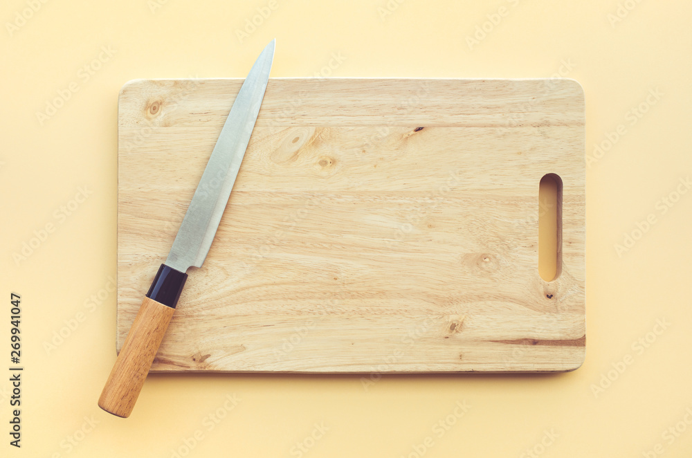 Knife on wooden chopping board on pastel color