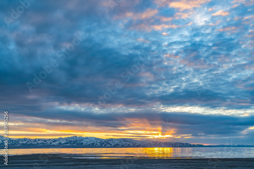 Lake and snow capped mountain underneath a sky filled with clouds at sunset