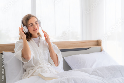 Happy pretty woman in earphones listening to music and singing while sitting on bed