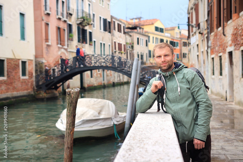Man in Venice. Portrait of handsome young man leaning against railing on walking street on narrow canal in Venice, Italy © dzmitrock87