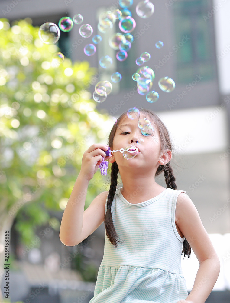Happy little girl playing soap bubbles in garden.