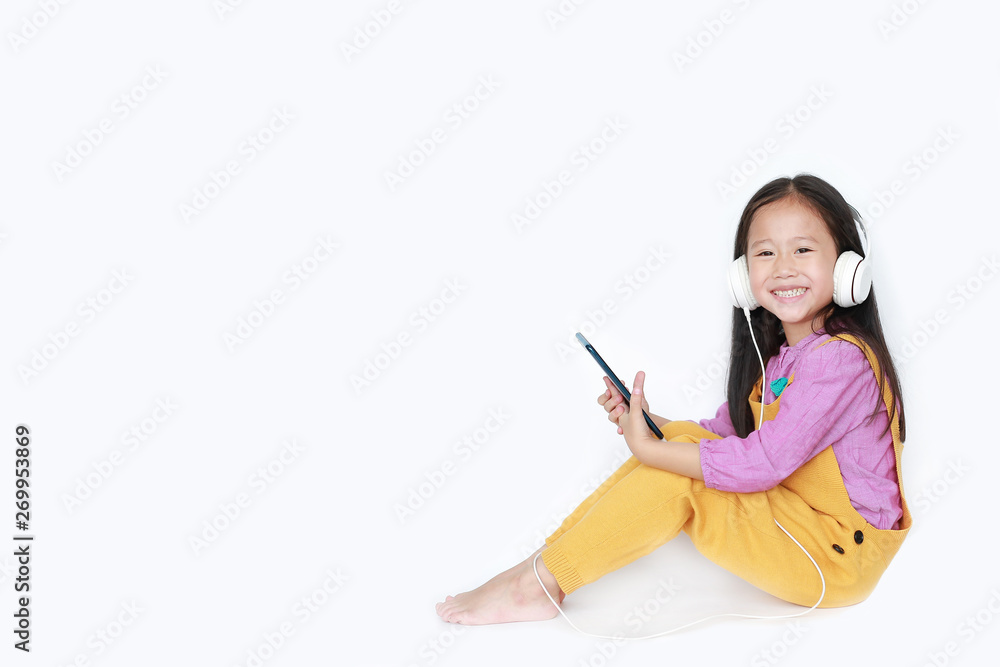 Pretty little Asian girl using smartphone to enjoys listening music with headphones isolated on white background with copy space. Pretty little Asian girl using smartphone to enjoys listening music with headphones isolated on white background with copy space.