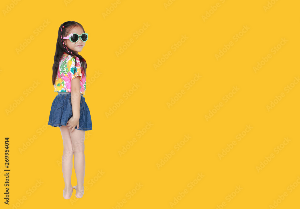 Happy little Asian kid girl wearing a flowers summer dress and sunglasses isolated on yellow background with copy space. Summer fashion kid concept. Happy little Asian kid girl wearing a flowers summer dress and sunglasses isolated on yellow background with copy space. Summer fashion kid concept.