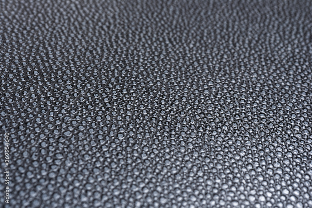 A macro or close-up shot of the visible and raised textured grain of a faux black leather with dramatic side lighting. A macro or close-up shot of the visible and raised textured grain of a faux black leather with dramatic side lighting.