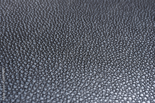 A macro or close-up shot of the visible and raised textured grain of a faux black leather with dramatic side lighting.