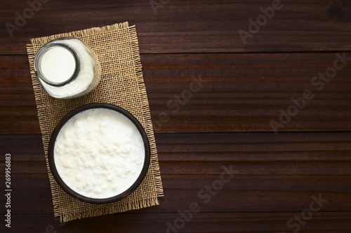 Kefirknollen in Milch in Schüssel und Milch in Flasche an der Seite, fotografiert mit natürlichem Licht