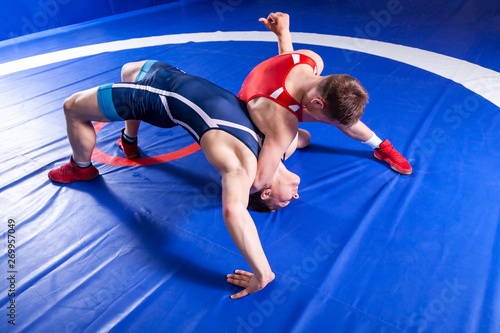 Two young sportsmens wrestlers in red and blue uniform wrestling against wrestling carpet, view above.