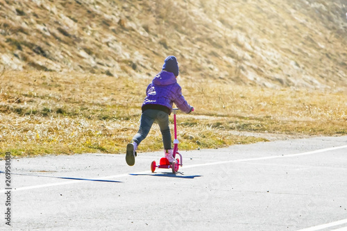 little girl riding a scooter on a sunny warm day in the park