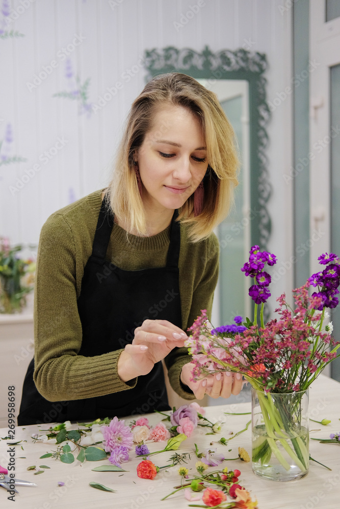 Young female flower seller laughs making up a flower arrangement. Flower shop. A smiling woman cut flowers and puts them in a vase. Young female flower seller laughs making up a flower arrangement. Flower shop. A smiling woman cut flowers and puts them in a vase.