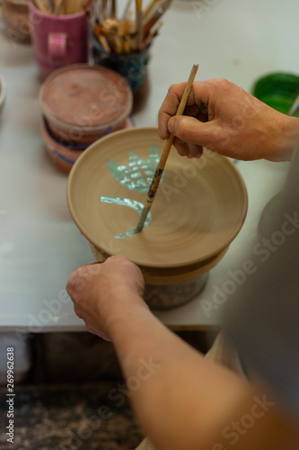 Focused man coloring and decorating dry clay plate