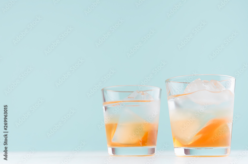 Tropical fresh layered cocktail with ice cubes, oranges liquor in misted shot glass on pastel blue background. Tropical fresh layered cocktail with ice cubes, oranges liquor in misted shot glass on pastel blue background.