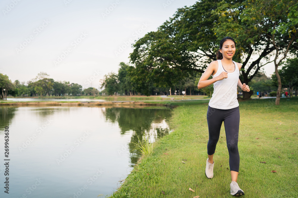 Healthy beautiful young Asian runner woman in sports clothing running and jogging on sidewalk near lake at park in the morning. Lifestyle fitness and active women exercise in urban city concept.