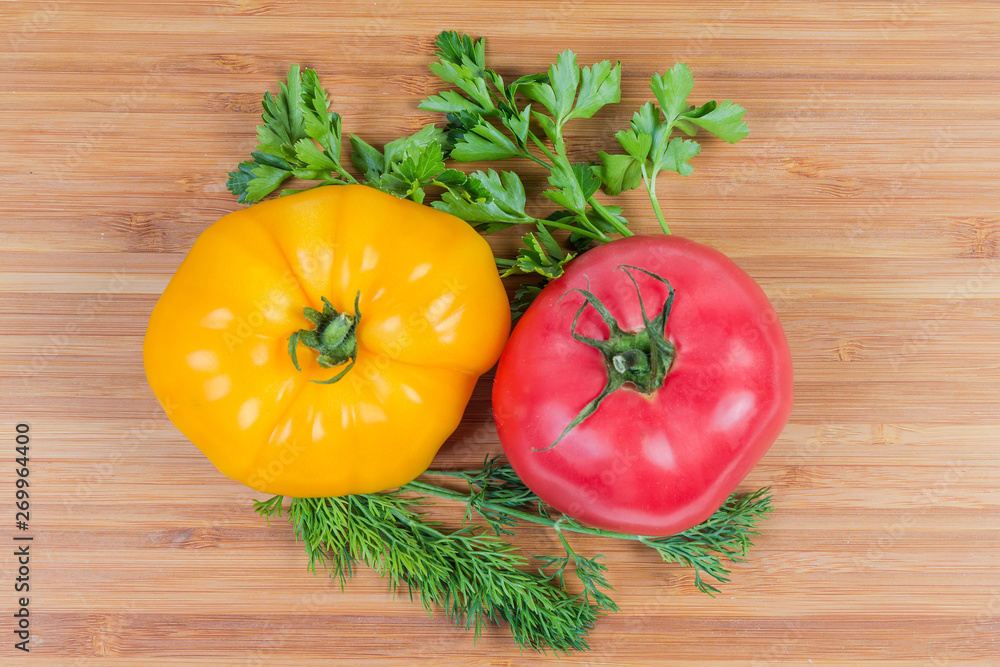 Pink and yellow tomatoes, greens on a wooden surface Pink and yellow tomatoes, greens on a wooden surface