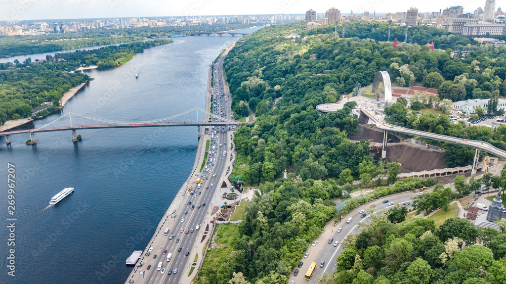 Fototapeta premium Aerial drone view of new pedestrian cycling park bridge construction, Dnieper river, hills, parks and Kyiv cityscape from above, city of Kiev skyline, Ukraine