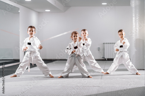 Small group of Caucasian kids in doboks practicing taekwondo and warming up for treining while standing barefoot. photo
