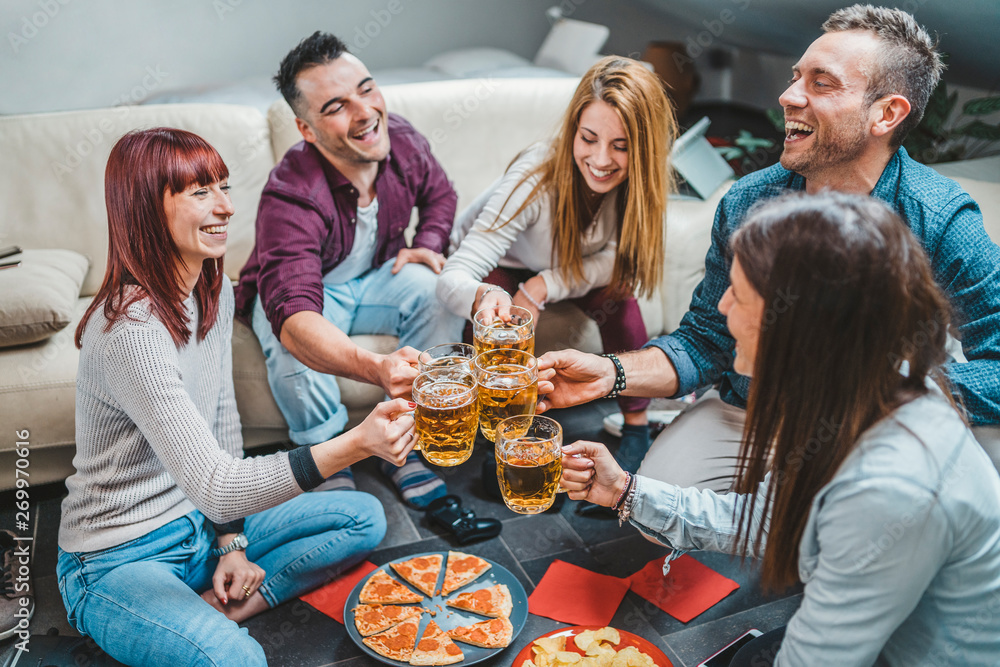 Group of friends toasting with a glass of beer while eating pizza - Millennials have fun together - Day of happiness between young men and women Group of friends toasting with a glass of beer while eating pizza - Millennials have fun together - Day of happiness between young men and women