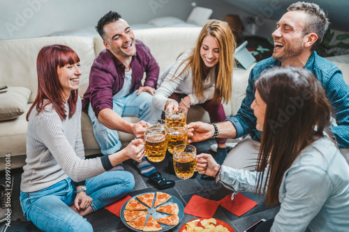 Group of friends toasting with a glass of beer while eating pizza - Millennials have fun together - Day of happiness between young men and women