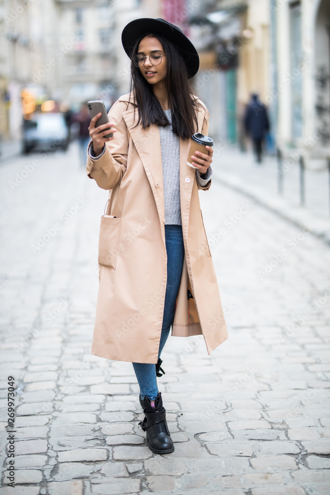 Beautiful smiling woman walking on city street from work with coffee cup and texting on mobile phone Beautiful smiling woman walking on city street from work with coffee cup and texting on mobile phone