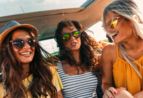 Three female friends enjoying traveling in the car. Sitting in rear seat and having fun on a road trip. © Zoran Zeremski