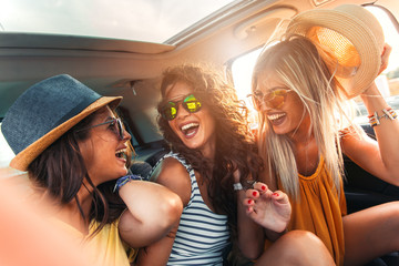 Three female friends enjoying traveling in the car. Sitting in rear seat and having fun on a road trip.