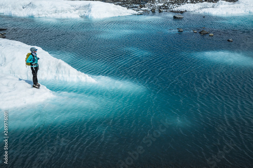 Guide standing on the edge of a deep blue lake on top of a glacier in Alaska. Supraglacial lake on white ice with moraine.