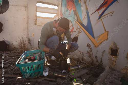 Graffiti artist filling graffiti color in aerosol spray while crouching photo