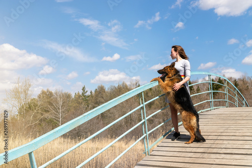 girl with her dog stand on the bridge and look into the distance at the horizon. the friendship of dogs and man.