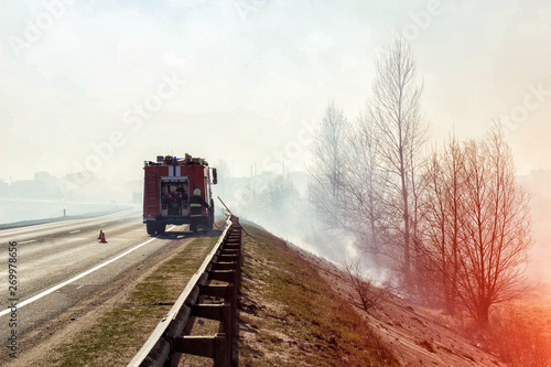 Fire truck with a firefighter on the road extinguishes a forest fire, heavy smoke, danger