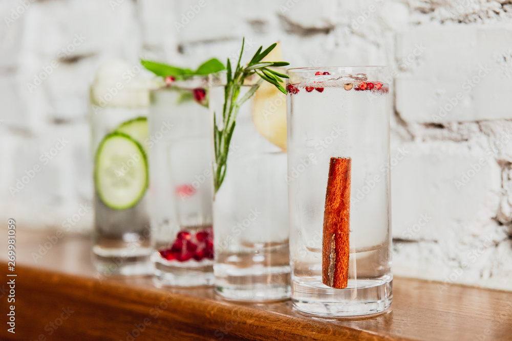 A horizontal image of 4 different refreshing gin and tonics in highball glasses. Cucumber and melon, pomegranate and basil, rosemary and apple, cinnamon and rose pepper. Selective focus. A horizontal image of 4 different refreshing gin and tonics in highball glasses. Cucumber and melon, pomegranate and basil, rosemary and apple, cinnamon and rose pepper. Selective focus.