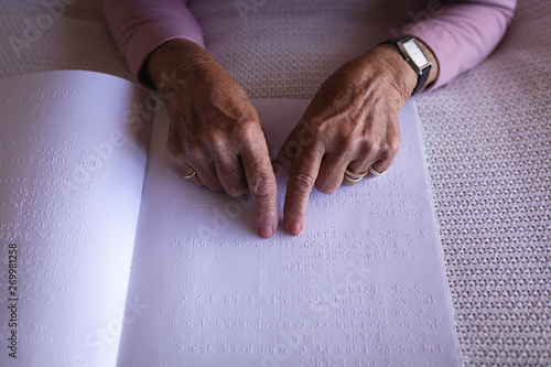 Blind active senior woman hands reading a braille book on bed in bedroom at home photo