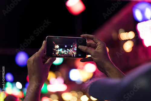 Young Asian traveler taking photo with mobile phone in pub and street road at night in Cambodia