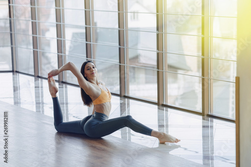 Fototapeta Naklejka Na Ścianę i Meble -  young attractive girl doing fitness exercises with yoga on the floor against the background of panoramic windows