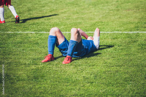 Football player lying on the lawn from pain after an injury - a rough game