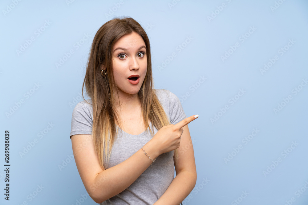 Teenager girl over isolated blue wall surprised and pointing side Teenager girl over isolated blue wall surprised and pointing side