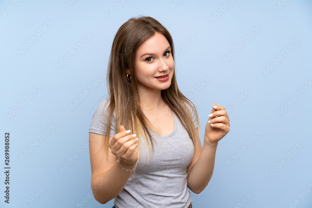 Teenager girl over isolated blue wall making money gesture Teenager girl over isolated blue wall making money gesture