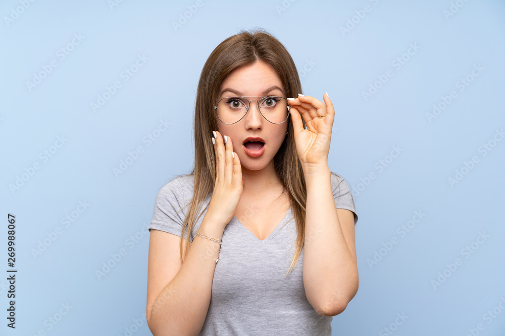 Teenager girl over isolated blue wall with glasses and surprised Teenager girl over isolated blue wall with glasses and surprised