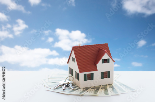 mortgage, real estate and property concept - close up of home or house model and money over blue sky and clouds background