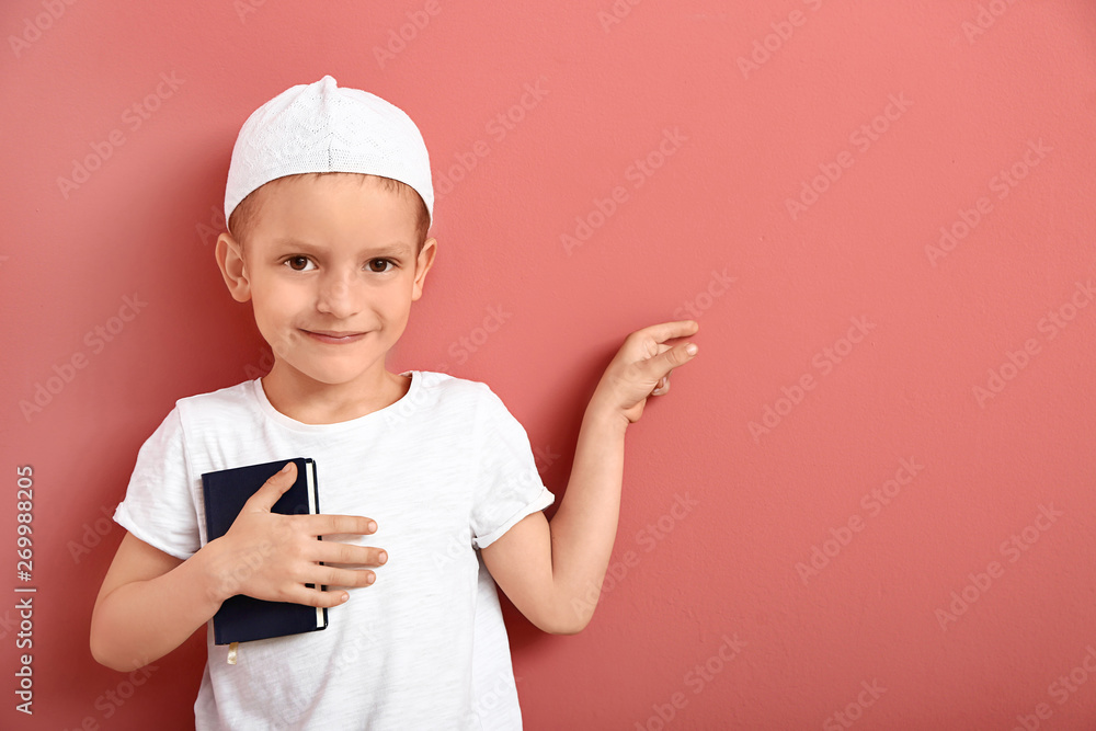 Little Muslim boy with Koran pointing at something on color background Little Muslim boy with Koran pointing at something on color background