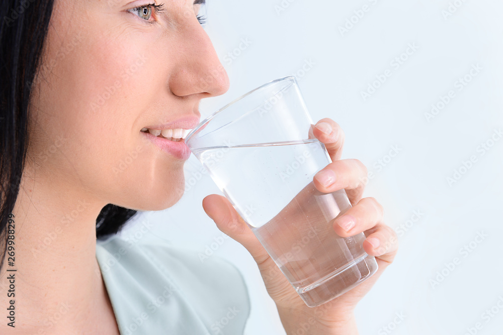 Woman drinking fresh water on light background Woman drinking fresh water on light background