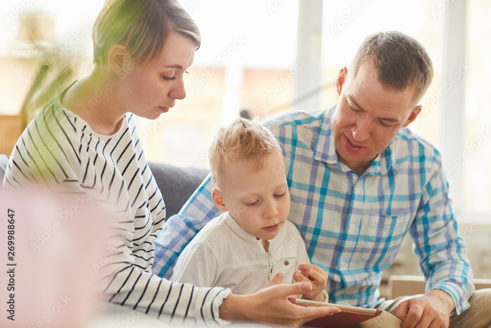 Pensive concentrated parents and their son using digital tablet for education and assisting him to learn lesson Pensive concentrated parents and their son using digital tablet for education and assisting him to learn lesson