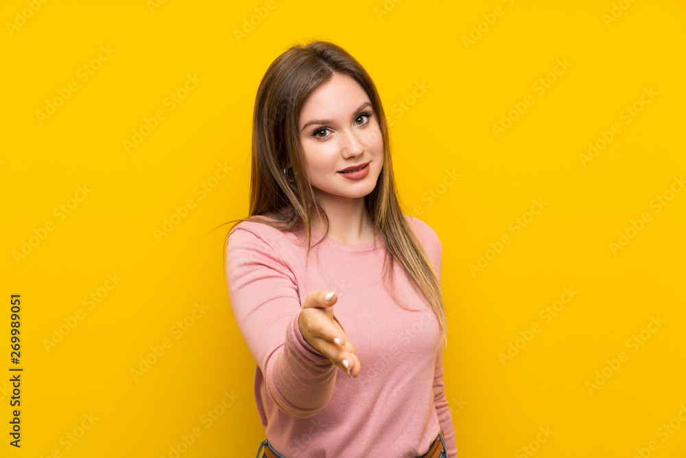 Teenager girl over isolated yellow background handshaking after good deal Teenager girl over isolated yellow background handshaking after good deal